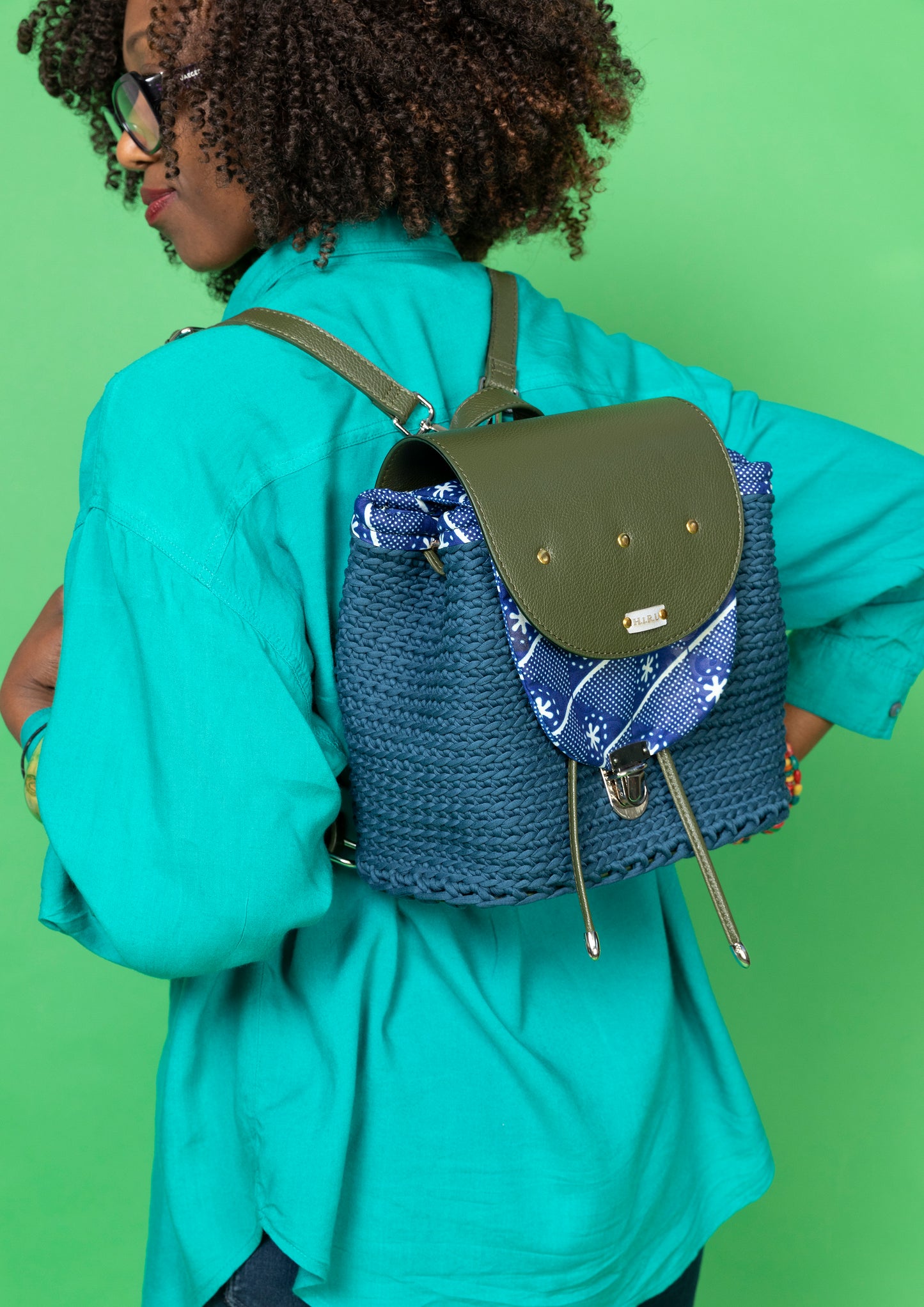 crocheted, dark blue and forest green bag, with an African style print. Model wearing the bag as a backpack, with straps over both shoulders.
