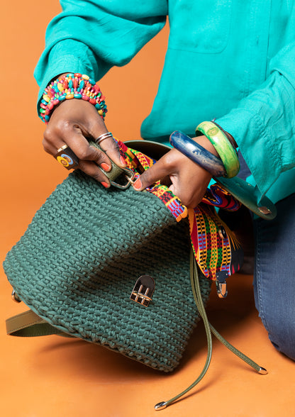 crocheted, forest/ oak green bag, with an African style print. Model shown adjusting straps.